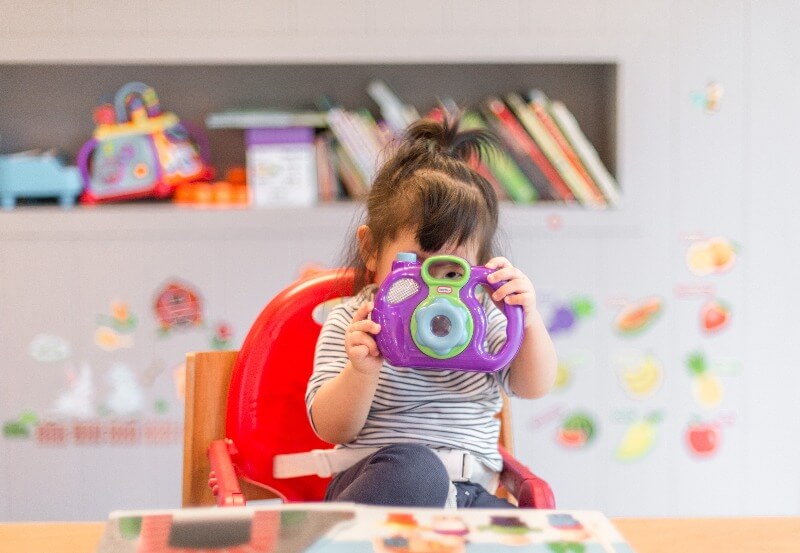 ポニーテールの子どもがおもちゃのカメラで遊んでいる